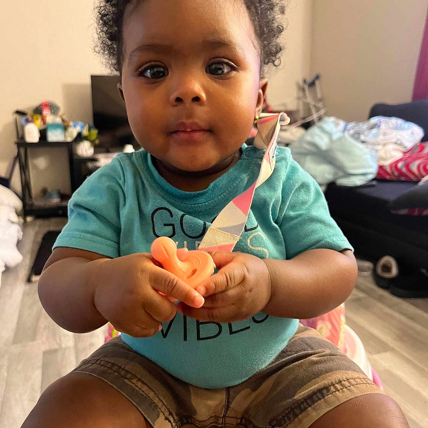 Fanta is registered to the contest to win money with this photo: baby, child, toddler, indoor, curly_hair, pacifier, clothing, shorts, shirt, person, furniture, living_room, floor, toy, sitting, cute, expression, home, childhood, young