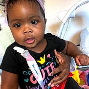 Fanta is registered to the contest to win money with this photo: baby, infant, child, headband, pink_bow, black_shirt, colorful_clothing, hand, indoor, baby_gear, curious_eyes, cute, sitting, person, portrait, skin, toddler, care, support, closeup