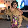 Popcorn is registered to the contest to win money with this photo: animal, barefoot, cat, child, dress, family_home, fluffy_cat, funny_pose, girl, holding, indoor, lamp, large_cat, living_room, orange_cat, pet, portrait, rug, smiling, television