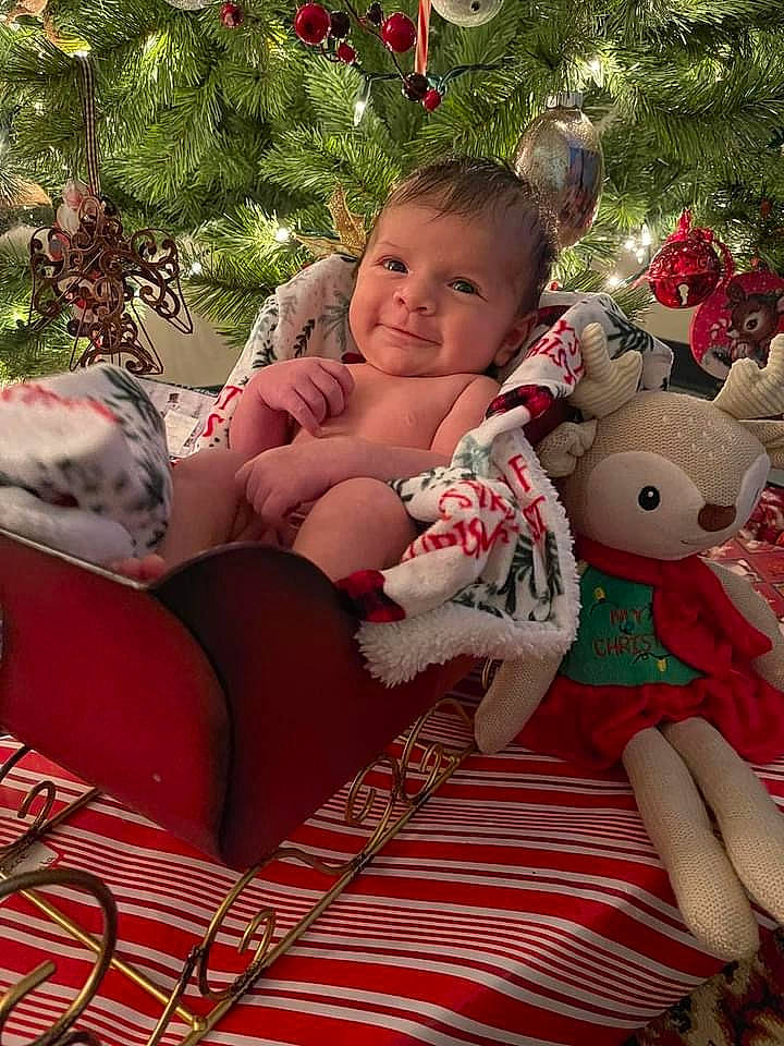Cecilia is registered to the contest to win money with this photo: baby, baby_toddler_clothing, christmas, christmas_decoration, christmas_eve, christmas_ornament, christmas_tree, comfort, event, grass, happy, holiday, joy, lap, ornament, person, red, skin, smile, thigh