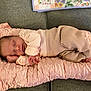 baby, newborn, sleeping, infant, pink_cushion, pastel_clothing, couch, blanket, floral_pattern, soft_fabric, cozy, resting, cute, peaceful, indoors, portrait, child, tiny_hands, tiny_feet, relaxing