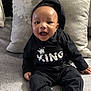 baby, child, smiling, hoodie, black_clothing, sitting, pillow, couch, happy, indoor, infant, cute, portrait, person, comfortable, cozy, young_child, apparel, fabric, expression