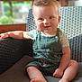 Côme participe au concours pour gagner de l'argent avec cette photo : baby, child, smiling, face, blue_eyes, green_overalls, short_hair, sitting, wicker_chair, armrest, bare_feet, indoor, natural_light, portrait, cute, happy, infant, casual_clothing, soft_background, wooden_wall