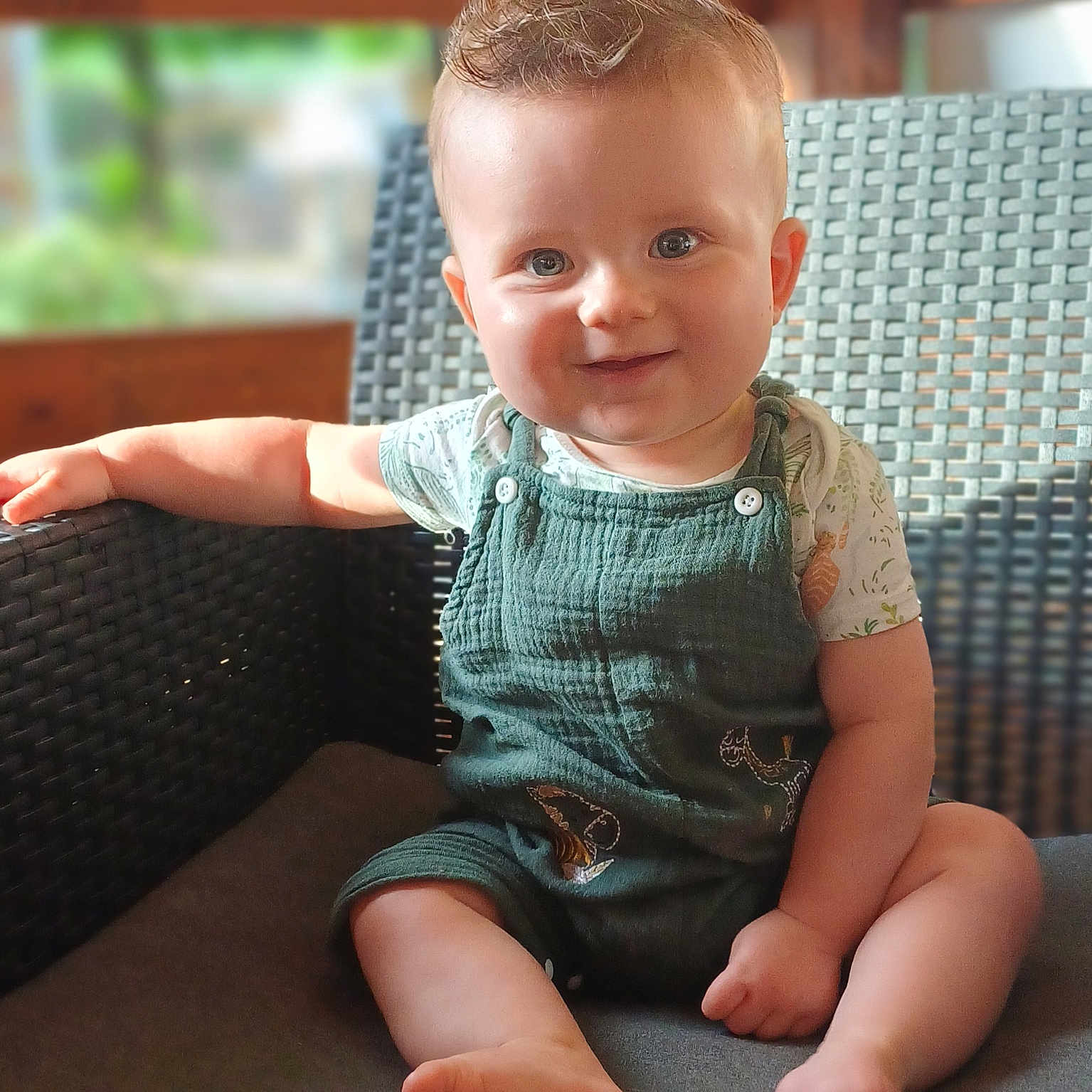 Côme participe au concours pour gagner de l'argent avec cette photo : armrest, baby, bare_feet, blue_eyes, casual_clothing, child, cute, face, green_overalls, happy, indoor, infant, natural_light, portrait, short_hair, sitting, smiling, soft_background, wicker_chair, wooden_wall