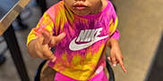 Brooklyn joined the competition — help win amazing prizes! child, girl, sitting, stool, colorful_clothing, nike_logo, hair_bows, indoor, curious_expression, shorts, sneakers, brown_skin, looking_up, hand_gesture, floor, table, blurry_background, portrait, casual, young