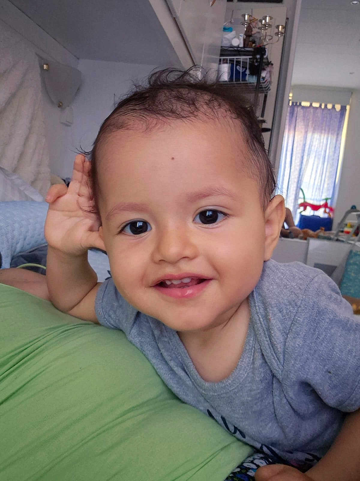 Gabriel a rejoint le concours — aidez-le/la à gagner de superbes lots ! toddler, child, smile, face, indoor, playful, curly_hair, grey_shirt, green_surface, toys, window, curtains, person, baby, happy, young_child, home, furniture, cute, portrait