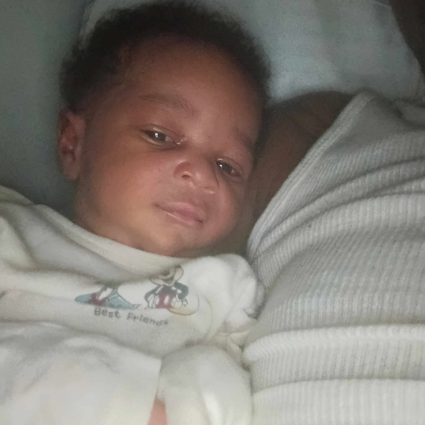 Ashton is registered to the contest to win money with this photo: baby, infant, child, face, hand, white_clothing, cartoon_print, sleepwear, resting, closeup, portrait, indoor, soft_lighting, fabric, texture, person, skin, head, curly_hair, cute