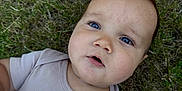 Smokey is registered to the contest to win money with this photo: baby, infant, blue_eyes, grass, outdoor, onesie, clothing, face, head, skin, curious, child, young, laying_down, nature, casual, expression, closeup, person, daylight