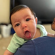 Katia joined the competition — help win amazing prizes! baby, child, tongue, face, person, skin, hair, green_shirt, shoulder, indoor, blurred_background, cute, expression, playful, closeup, holding, infant, young_child, portrait, human