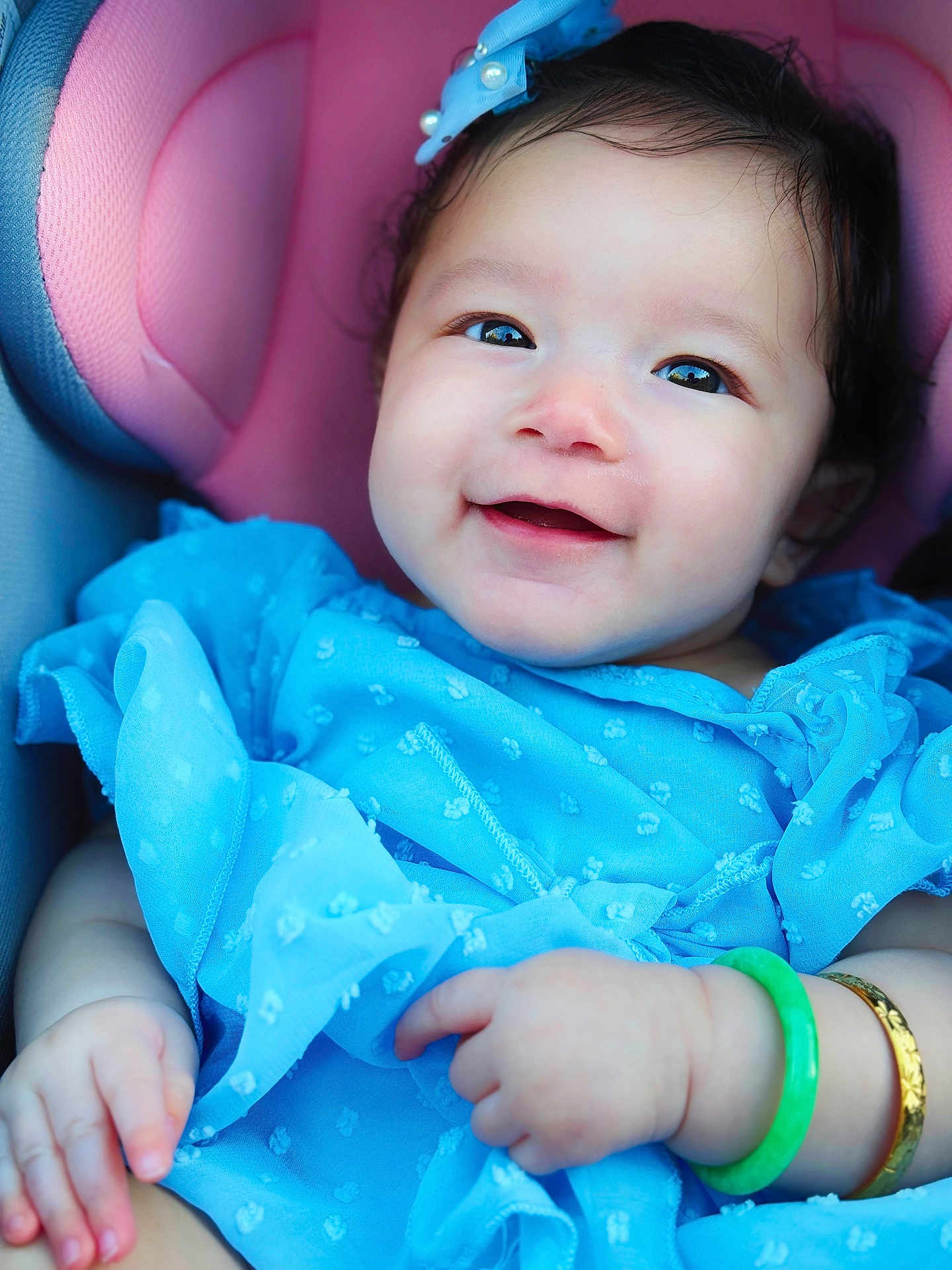 Katia is registered to the contest to win money with this photo: baby, smiling, blue_dress, headband, bracelet, pink_cushion, seat, child, cute, happy, portrait, infant, skin, hand, face, apparel, accessory, closeup, young, adorable