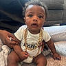 Roman is registered to the contest to win money with this photo: baby, infant, child, portrait, sitting, wide_eyed, curly_hair, gold_chain, jewelry, white_shirt, diaper, carpet, blanket, couch, living_room, indoor, adult_hand, family, closeup, photography