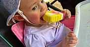 Athena is registered to the contest to win money with this photo: baby, child, infant, stroller, sun_hat, ice_cream, frozen_treat, eating, outdoor, summer, portrait, face, eyes, smiling, clothing, purple_shirt, highchair_tray, camping, chairs, sunlight