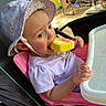 baby, child, infant, stroller, sun_hat, ice_cream, frozen_treat, eating, outdoor, summer, portrait, face, eyes, smiling, clothing, purple_shirt, highchair_tray, camping, chairs, sunlight