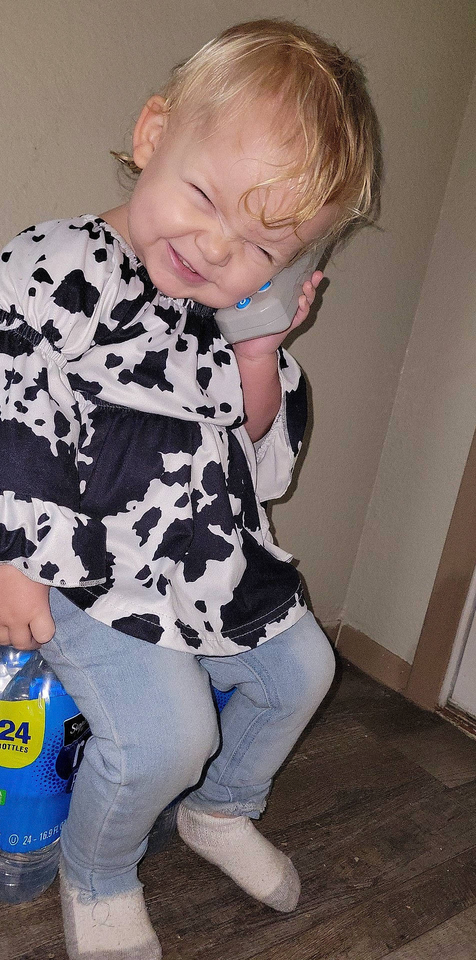 Paisley is registered to the contest to win money with this photo: baby_toddler_clothing, blond, cheek, child, cool, denim, eye, facial_expression, flooring, fun, hairstyle, happy, pattern, person, sitting, sleeve, smile, standing, t_shirt, thigh