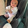 baby, car_seat, child, pink_hat, white_clothing, tongue_out, smiling, car_interior, seatbelt, hand, cute, infant, person, portrait, sitting, warm_clothing, playful, young_child, car, seat