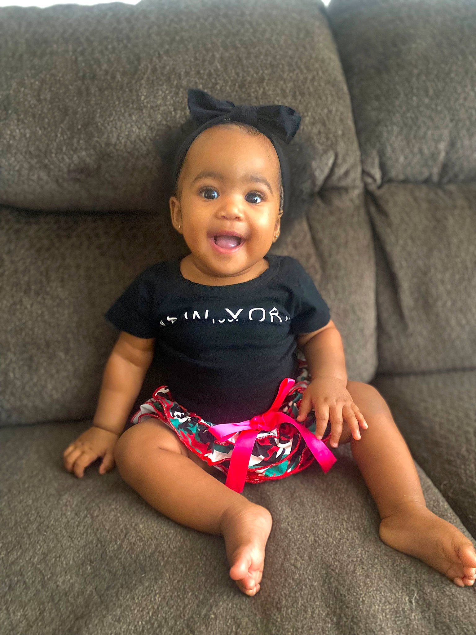 Aaliyah is registered to the contest to win money with this photo: baby, baby_toddler_clothing, barefoot, comfort, couch, finger, floor, flooring, head, human_leg, joint, leg, lip, neck, person, skin, sleeve, smile, t_shirt, thigh