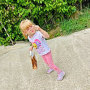 Lucy joined the competition — help win amazing prizes! blonde_hair, bushes, casual_clothing, child, concrete, curious, daylight, girl, greenery, leggings, outdoor, paper_bag, pink, pink_glasses, playful, sidewalk, sneakers, spongebob, standing, tshirt