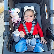 Nova joined the competition — help win amazing prizes! toddler, child, stroller, headband, red_shirt, blue_jeans, unicorn_toy, bottle, happy, smiling, curly_hair, outdoor, seatbelt, baby, person, cute, daylight, casual_clothing, playful, comfort