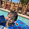 child, pool, water, floaties, swimming_ring, wet_hair, sunny_day, outdoor, palm_trees, blue_sky, toy_story, smiling, summer, recreation, leisure, swimwear, playful, fun, vacation, young