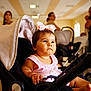 baby, child, stroller, pink_dress, bow, indoor, people, woman, blurred_background, seated, infant, portrait, cute, young_child, casual_clothing, expression, light, room, soft_light, focus