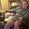 Tiki joined the competition — help win amazing prizes! man, cat, armchair, leather, remote_control, lamp, window, curtains, pillow, shorts, hoodie, glasses, carpet, indoor, relaxing, pet, feline, casual, evening, home