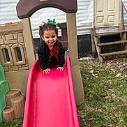 Armonie is registered to the contest to win money with this photo: child, toddler, smiling, slide, playground, outdoor, grass, leaves, plastic_playset, house, door, steps, climbing, fun, happy, casual_clothing, black_jacket, red_shirt, daylight, backyard