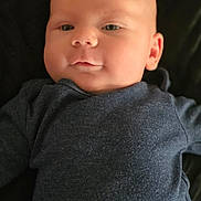 Ryder is registered to the contest to win money with this photo: baby, infant, face, portrait, child, clothing, dark_background, expression, skin, head, eyes, nose, mouth, ear, young, cute, cozy, lying_down, soft_light, closeup