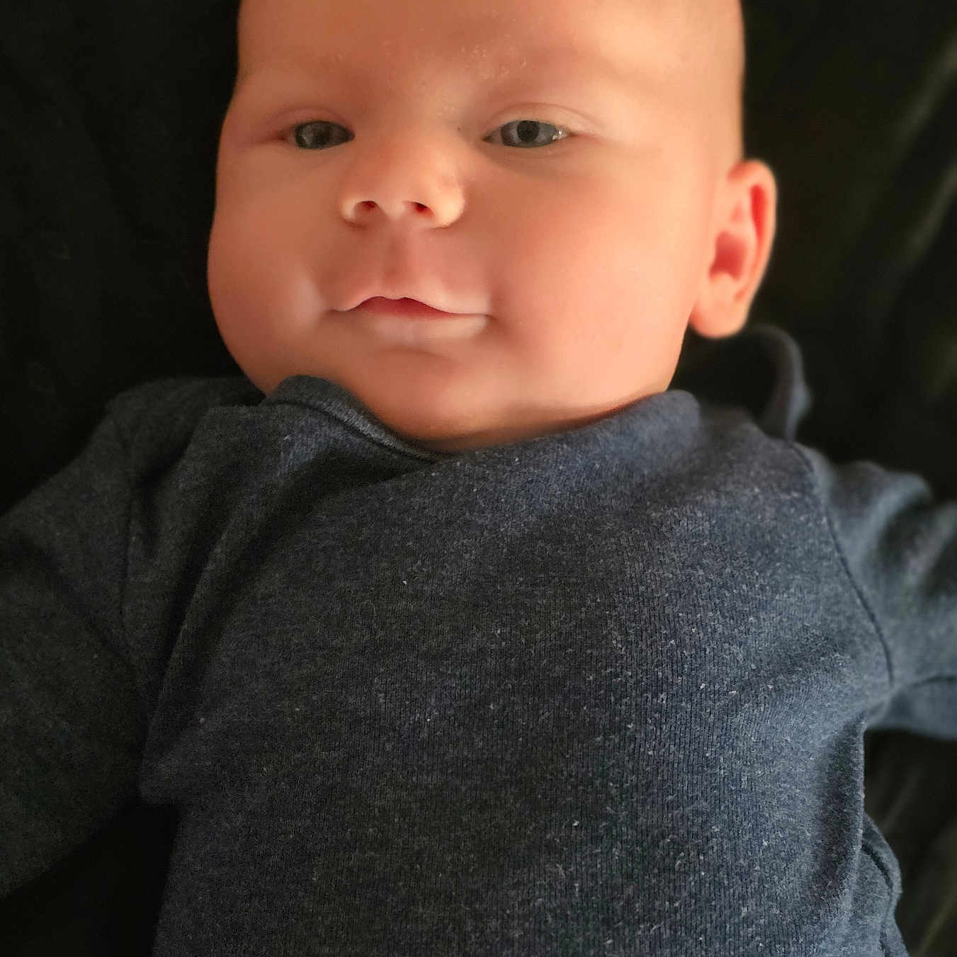 Ryder is registered to the contest to win money with this photo: baby, infant, face, portrait, child, clothing, dark_background, expression, skin, head, eyes, nose, mouth, ear, young, cute, cozy, lying_down, soft_light, closeup