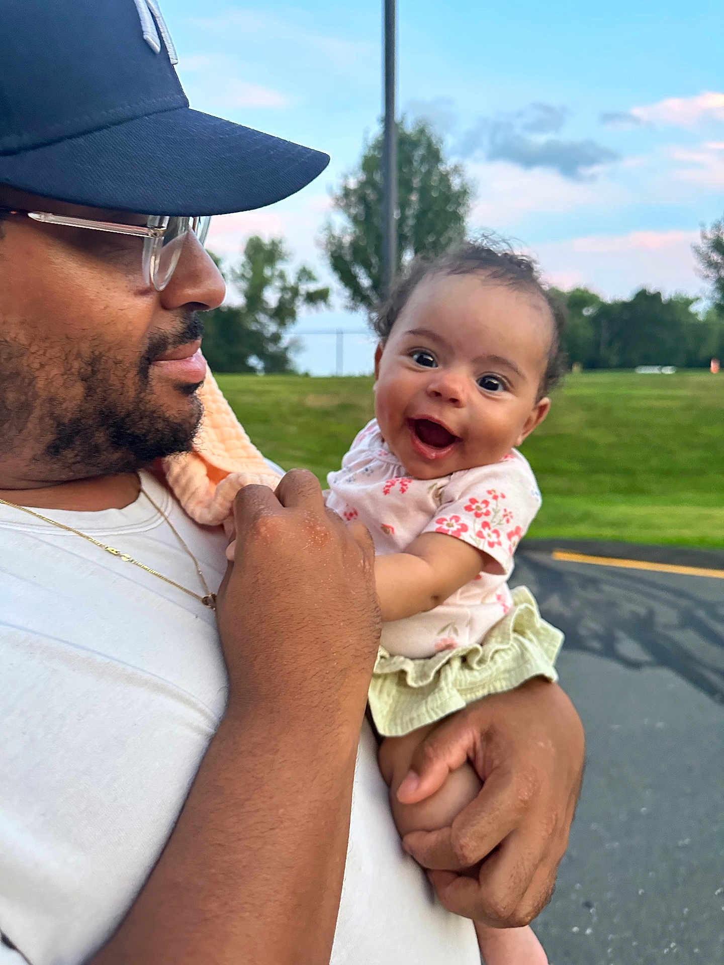Eliana joined the competition — help win amazing prizes! baby, child, adult, man, glasses, cap, smile, happy, outdoor, grass, sky, holding, person, casual_clothing, nature, daylight, portrait, parent, affection, cute