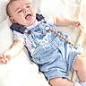 Baylor is registered to the contest to win money with this photo: baby, blanket, child, clothing, cute, denim_overalls, hand, happy, head, indoors, infant, lying_down, pacifier_clip, person, portrait, skin, smiling, socks, soft_light, white_shirt