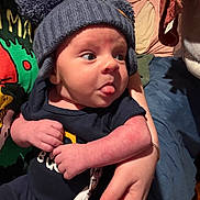 Baylor is registered to the contest to win money with this photo: baby, infant, hat, pom_poms, tongue_out, hand, clothing, person, holding, indoor, blanket, bed, nail_polish, cute, expression, face, skin, warm_lighting, portrait, newborn