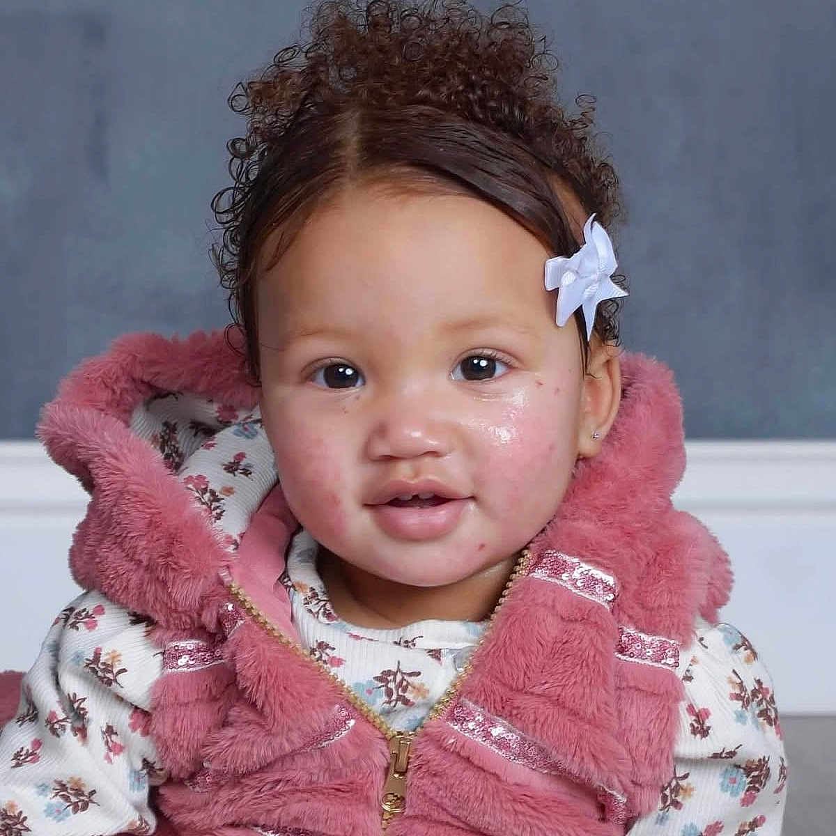 Veriya joined the competition — help win amazing prizes! child, toddler, curly_hair, bow, pink_vest, floral_shirt, face, portrait, indoor, cute, smile, young_child, cozy_clothing, curious, baby, person, fashion, hairstyle, expression, studio_photo