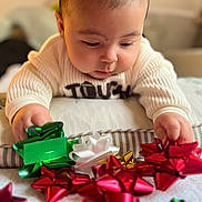 Nathan is registered to the contest to win money with this photo: baby, child, face, hands, sweater, gift_bow, red_bow, green_bow, white_bow, holiday, christmas, curious, closeup, indoor, soft_light, table, decorations, focus, portrait, candid