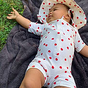 Daïanna a rejoint le concours — aidez-le/la à gagner de superbes lots ! baby, child, grass, blanket, outdoor, hat, polka_dot, white_clothing, red, skin, legs, arm, nature, infant, cute, relaxed, exploring, summer, sunlight, lying_down