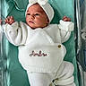 baby, newborn, infant, knitted_clothing, white_outfit, headband, bow, crib, hospital, blanket, lying_down, cute, small_hands, tiny_feet, peaceful, curious, portrait, indoors, child, person