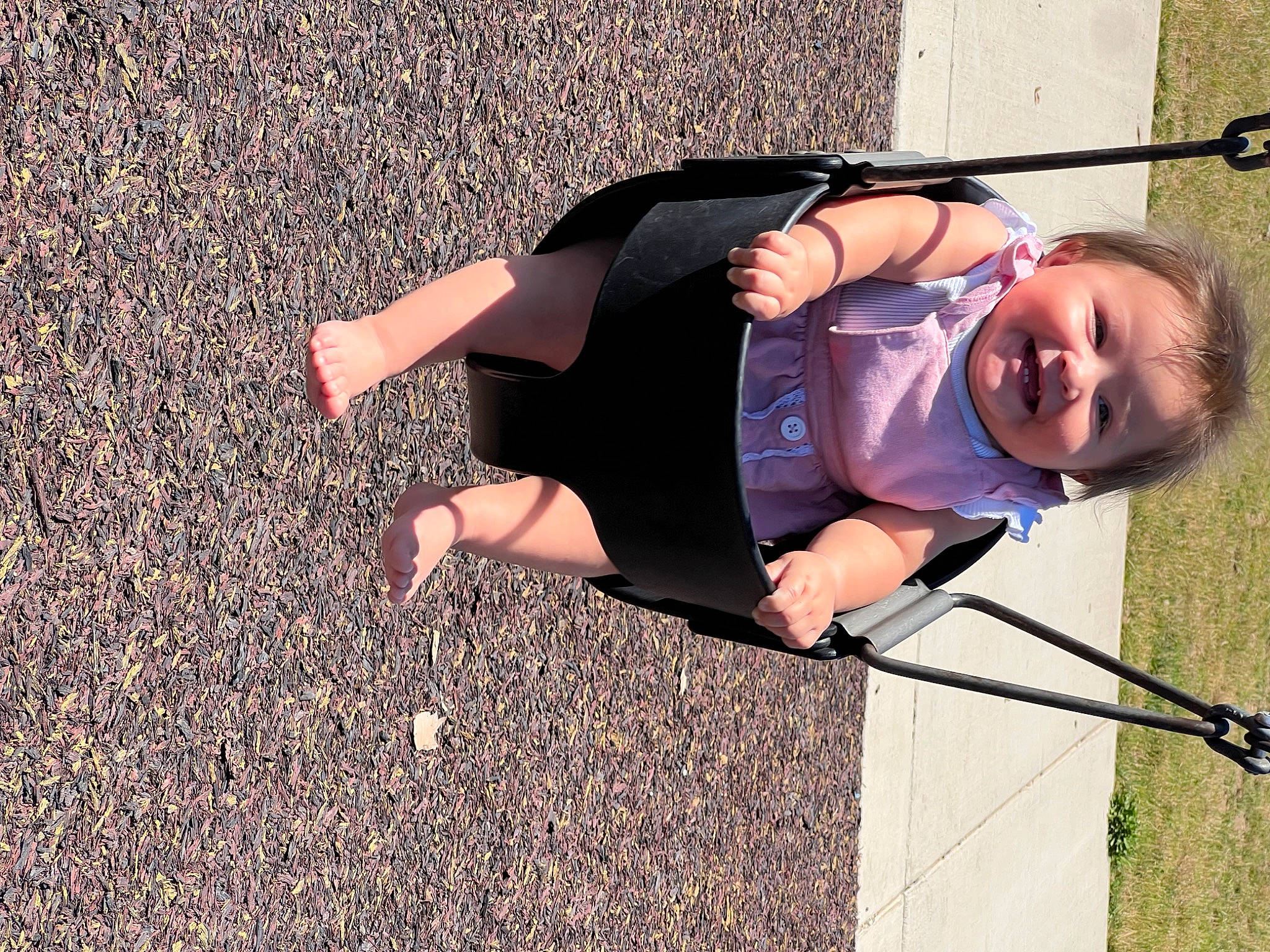 Ella is registered to the contest to win money with this photo: asphalt, child, eyewear, fun, grass, happy, human_leg, joy, leisure, people_in_nature, person, personal_protective_equipment, play, recreation, road_surface, shadow, sitting, smile, soil, toddler