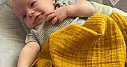 John is registered to the contest to win money with this photo: baby, infant, blanket, yellow_blanket, baby_seat, cushion, smiling, reaching_hand, indoor, cozy, clothing, cute, child, portrait, relaxed, home, soft_light, skin, head, face