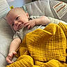 baby, infant, blanket, yellow_blanket, baby_seat, cushion, smiling, reaching_hand, indoor, cozy, clothing, cute, child, portrait, relaxed, home, soft_light, skin, head, face
