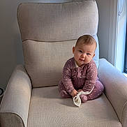 Ava is registered to the contest to win money with this photo: baby, child, armchair, indoor, onesie, polka_dot, fabric, furniture, curious, sitting, cloth, window, light, portrait, cute, infant, soft_lighting, home, cozy, smile