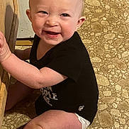 Chester is registered to the contest to win money with this photo: baby, child, smiling, sitting, black_shirt, diaper, floor, wooden_surface, happy, cute, infant, indoor, person, face, skin, legs, arms, expression, young, playful