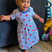 Harley Marie is registered to the contest to win money with this photo: toddler, child, smiling, dress, striped_dress, strawberry_pattern, barefoot, indoor, wood_floor, couch, toy, colorful_toys, happy, walking, person, young_child, playful, home, cute, portrait