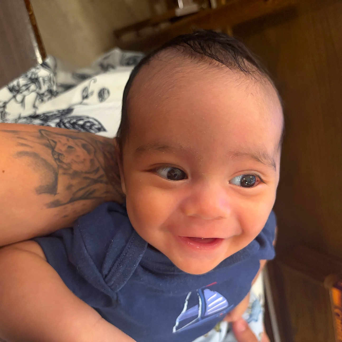 Lucas joined the competition — help win amazing prizes! baby, smile, tattoo, arm, blue_clothing, indoor, wooden_furniture, blanket, pattern, person, face, child, cute, happy, infant, closeup, portrait, human, skin, eyes