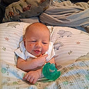 Uriah is registered to the contest to win money with this photo: baby, infant, pacifier, blanket, pillow, dinosaur_pattern, clothing, face, hand, indoor, bedroom, cute, expression, newborn, resting, cozy, portrait, child, person, soft_fabric