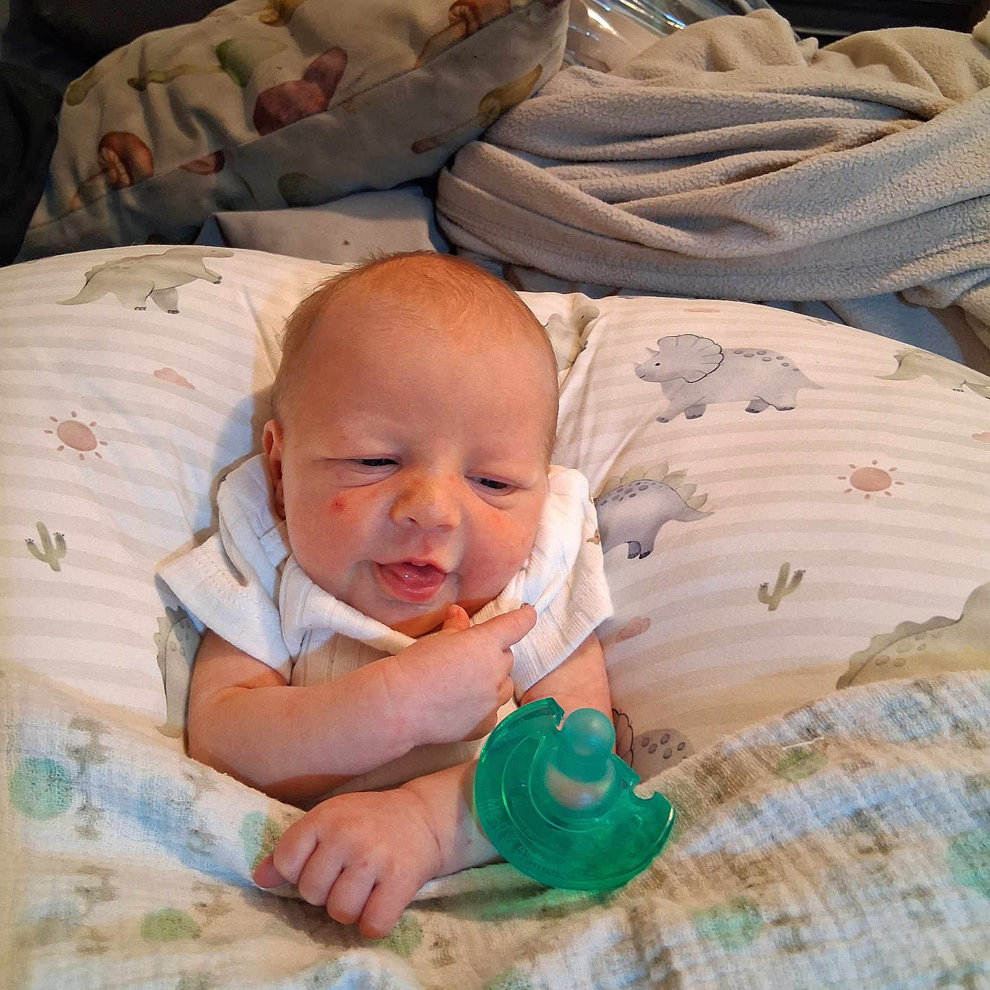 Uriah is registered to the contest to win money with this photo: baby, bedroom, blanket, child, clothing, cozy, cute, dinosaur_pattern, expression, face, hand, indoor, infant, newborn, pacifier, person, pillow, portrait, resting, soft_fabric