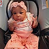baby, infant, child, car_seat, pink_outfit, headband, bow, dress, frills, sitting, portrait, face, smiling, hands, indoor, vehicle, safety_harness, carriage, fashionable, photography