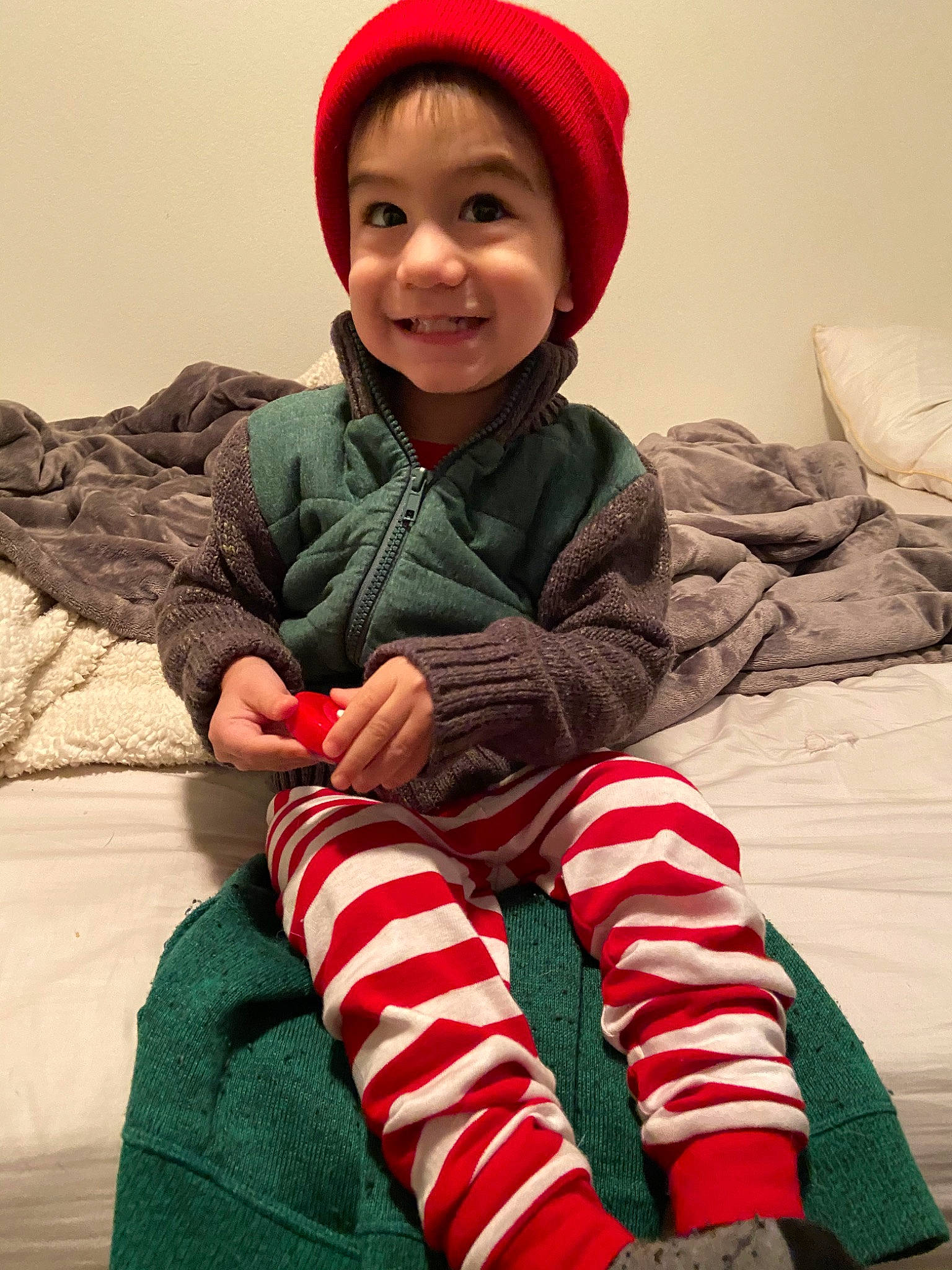 Dale is registered to the contest to win money with this photo: child, christmas, christmas_eve, fictional_character, headgear, holiday, joy, knit_cap, outerwear, pajamas, person, sitting, sleeve, smile, toddler, wool