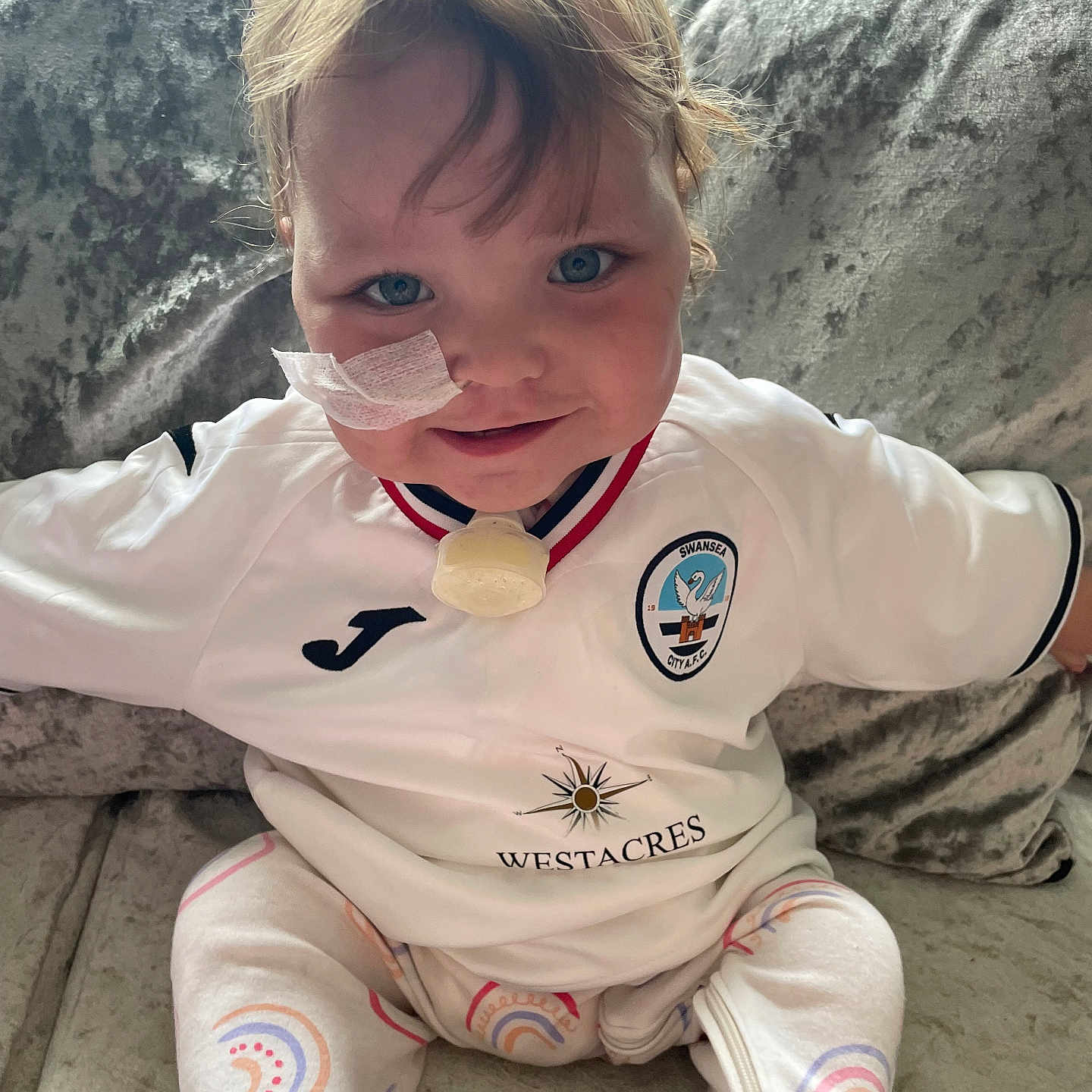 Ava is registered to the contest to win money with this photo: animal, baby, blonde, bodypart, clothing, costume, couch, cushion, face, finger, furniture, hair, hand, head, homedecor, pajamas, pants, person, photography, portrait