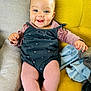 baby, child, smiling, sitting, couch, yellow_cushion, pink_tights, black_dress, face, blue_eyes, happy, indoors, plush_blanket, hand, legs, head, cute, comfort, expression, clothing