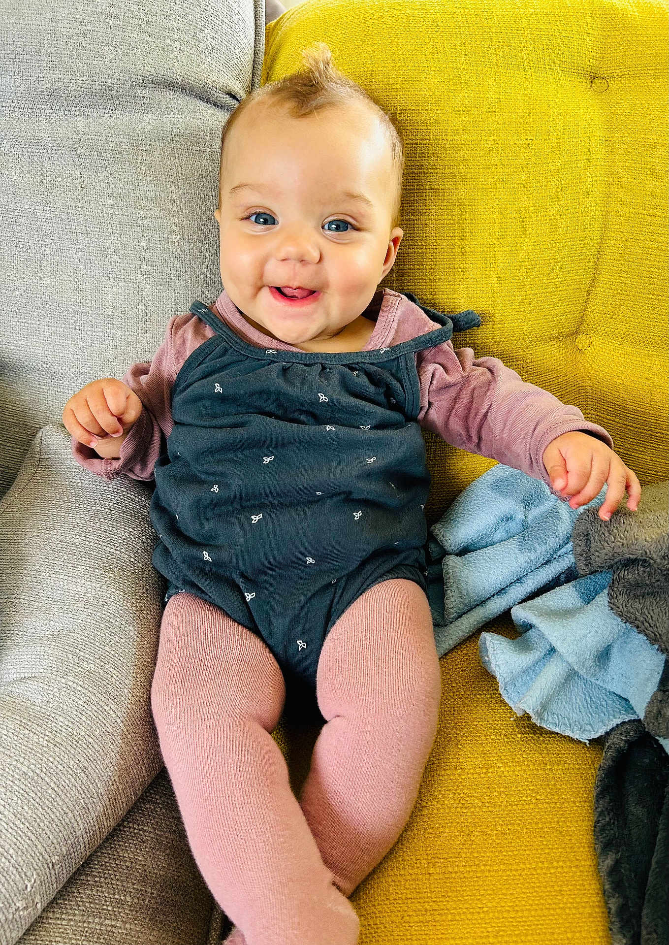 Camille participe au concours pour gagner de l'argent avec cette photo : baby, child, smiling, sitting, couch, yellow_cushion, pink_tights, black_dress, face, blue_eyes, happy, indoors, plush_blanket, hand, legs, head, cute, comfort, expression, clothing
