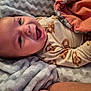 baby, smiling, blanket, onesie, pretzel_pattern, cozy, happy, infant, child, face, portrait, lying_down, cute, skin, head, hand, soft_texture, bed, comfort, sleepwear
